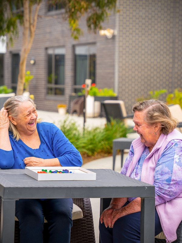 BAPTCARE COASTHAVEN Residents joking while playing a board game outside in the courtyard