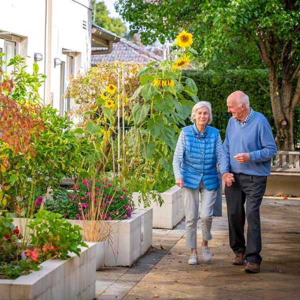 BAPTCARE HEDLEY SUTTON Resident couple hand-in-hand chatting and taking a walk together in the courtyard garden