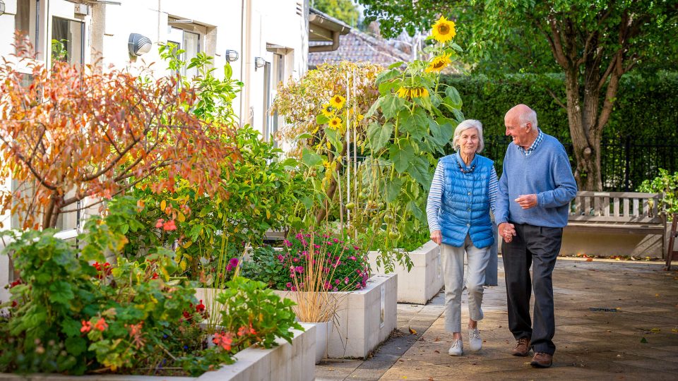 BAPTCARE HEDLEY SUTTON Resident couple hand-in-hand chatting and taking a walk together in the courtyard garden