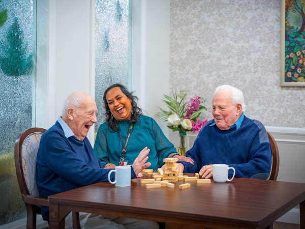 BAPTCARE HEDLEY SUTTON Resident friends playing Jenga as it falls over, much laughter with a staff member looking on