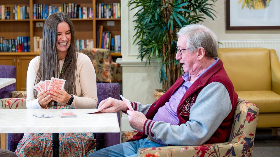 BAPTCARE HERITAGE MANOR Resident playing cards with a staff member near the library