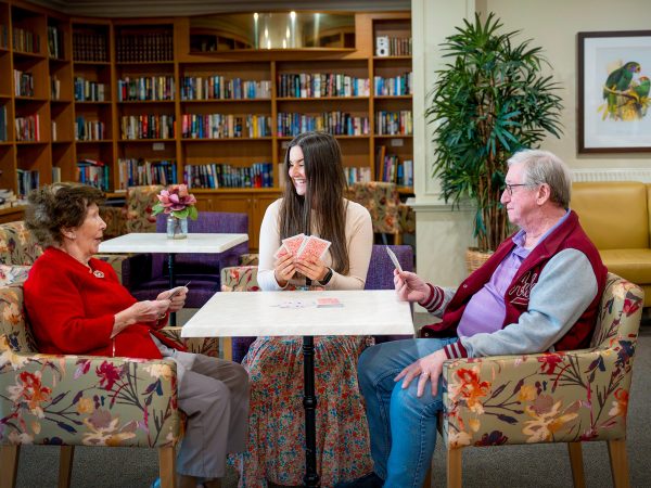 BAPTCARE HERITAGE MANOR Resident friends playing cards with a staff member near the library