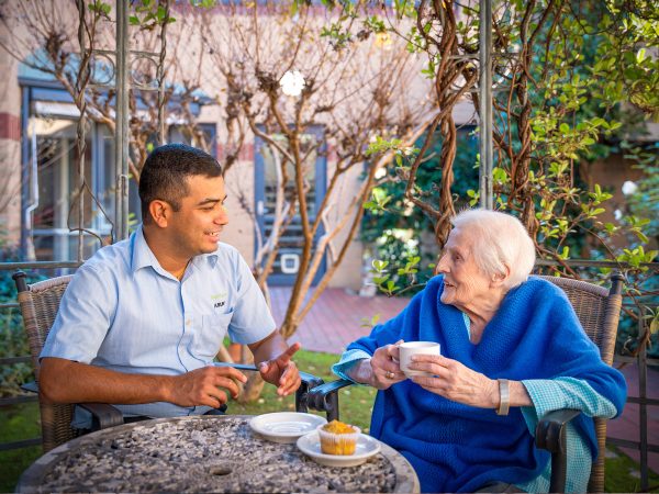 BAPTCARE KARANA Resident with staff member sharing conversation and a cupcake with tea