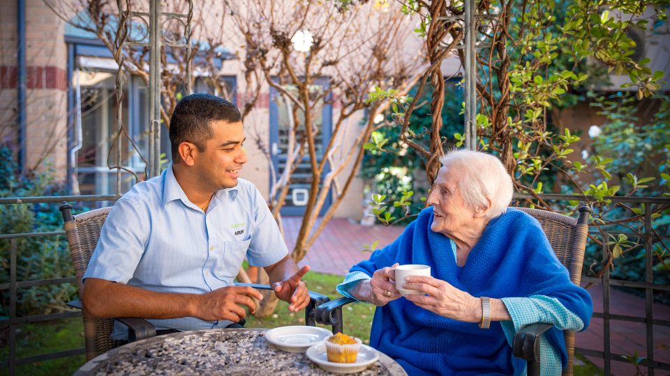 BAPTCARE KARANA Resident with staff member sharing conversation and a cupcake with tea