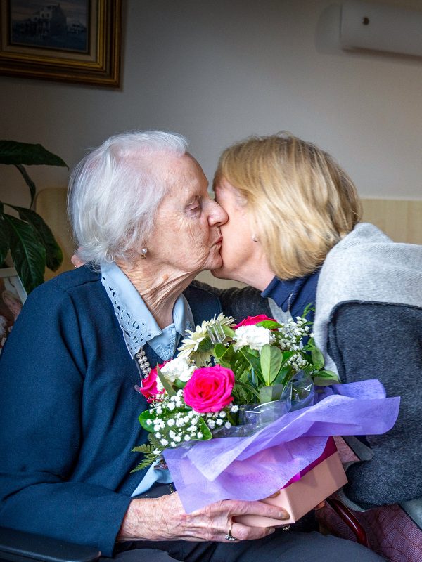 BAPTCARE PENINSULA VIEW resident in her room with her daughter giving her flowers and a kiss