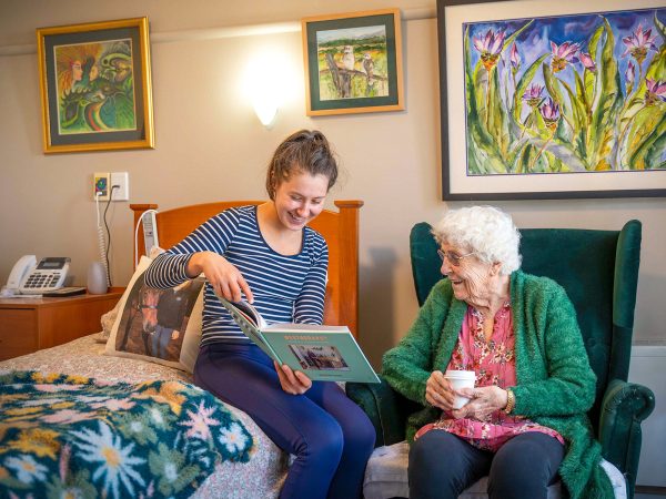 BAPTCARE WESTHAVEN Resident mother and her granddaughter sharing a book and laughing in her room