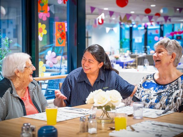 BAPTCARE Wyndham Lodge two resident friends at an event in dining room sharing a laugh with a staff member