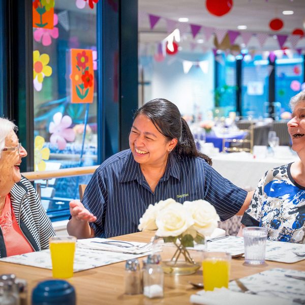 BAPTCARE Wyndham Lodge two resident friends at an event in dining room sharing a laugh with a staff member