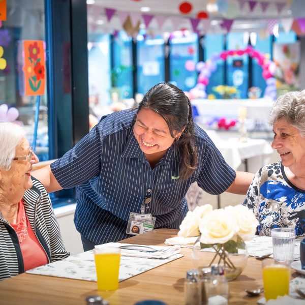 BAPTCARE Wyndham Lodge two resident friends at an event in dining room sharing a laugh with a staff member