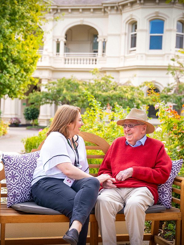 Two people chatting at Hedley Sutton on a bench in the Garden Courtyard