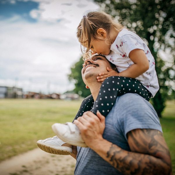 FAMILY COMMUNITY Young dad with young daughter on his shoulders looking up and smiling