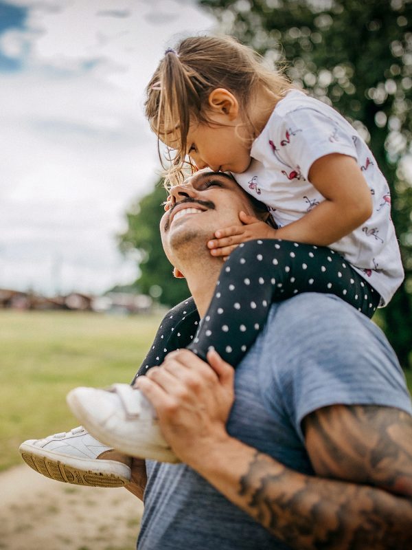 FAMILY COMMUNITY Young dad with young daughter on his shoulders looking up and smiling