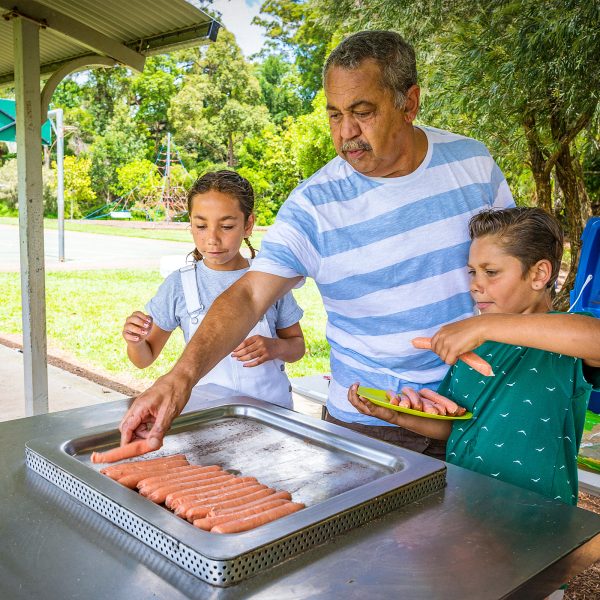 FAMILY COMMUNITY Older dad cooking sausages with his three grand children in the park