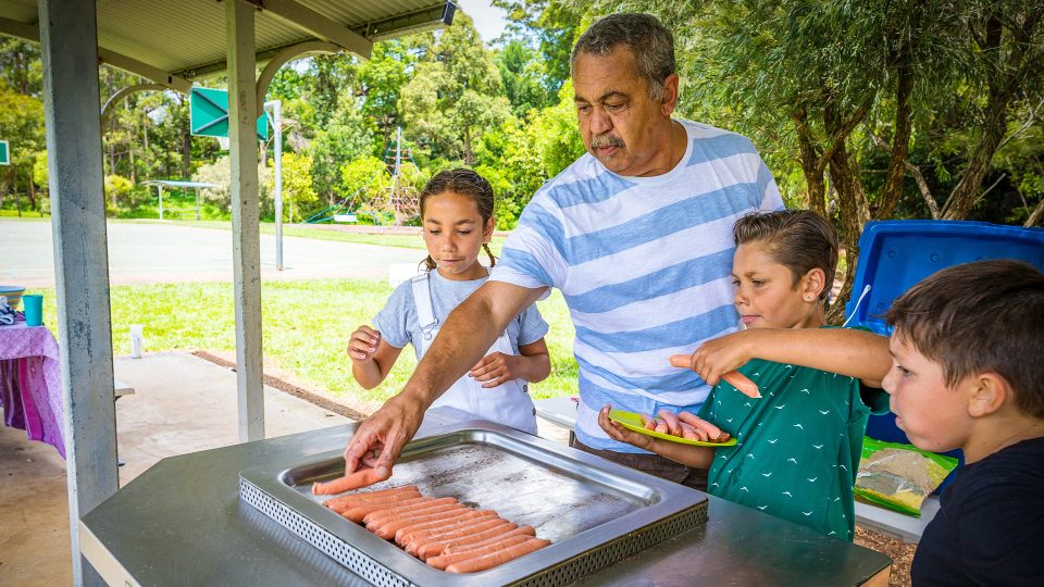 FAMILY COMMUNITY Older dad cooking sausages with his three grand children in the park