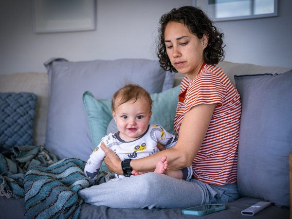 FAMILY COMMUNITY Young pensive mum and her infant daughter sitting on a couch together