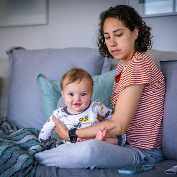 FAMILY COMMUNITY Young pensive mum and her infant daughter sitting on a couch together