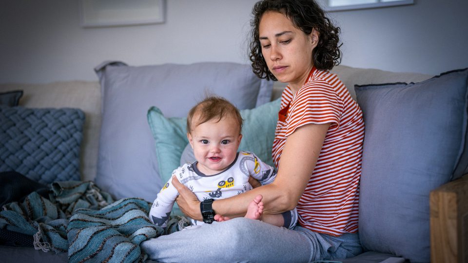 FAMILY COMMUNITY Young pensive mum and her infant daughter sitting on a couch together