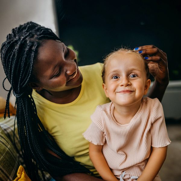 Young single woman foster carer with young girl in her care sitting on her lap making a cute face at the camera