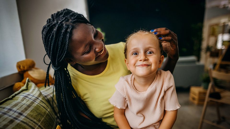 Young single woman foster carer with young girl in her care sitting on her lap making a cute face at the camera