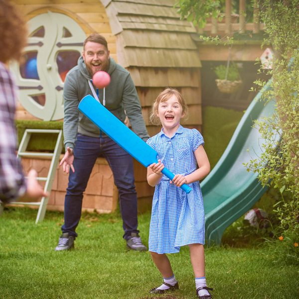 Male and female couple foster carers playing a game of cricket with a young girl in their care holding a bat about to hit a ball