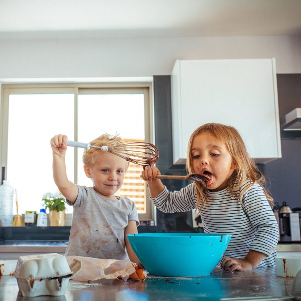 Two young foster care siblings making a cake in the kitchen licking the spoon and spatula