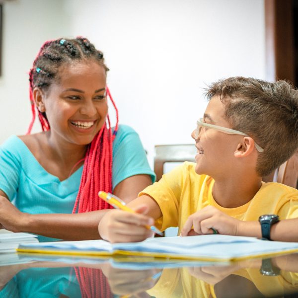 Young single woman foster carer helping a young boy in her care with his homework