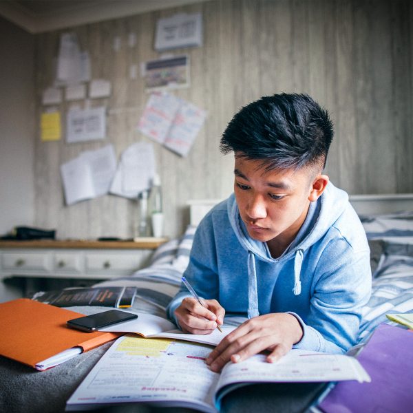 KINSHIP CARE Asian teenage boy doing his homework in his bedroom