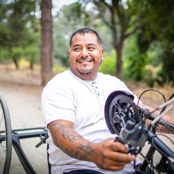 DISABILITY middle aged male amputee on a hand crank bicycle smiling as he bikes down a dirt road