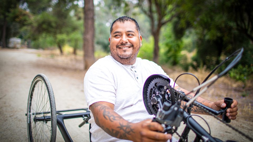 DISABILITY middle aged male amputee on a hand crank bicycle smiling as he bikes down a dirt road