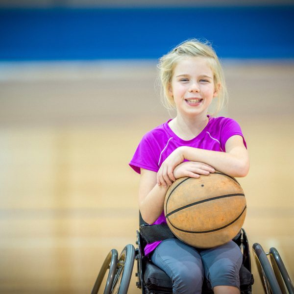 DISABILITY girl in a wheelchair playing basketball and smiling at camera