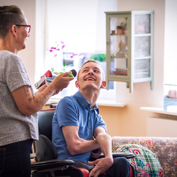 DISABILITY carer help feeding a young man wheelchair bound with cerebral palsy both sharing a laugh together