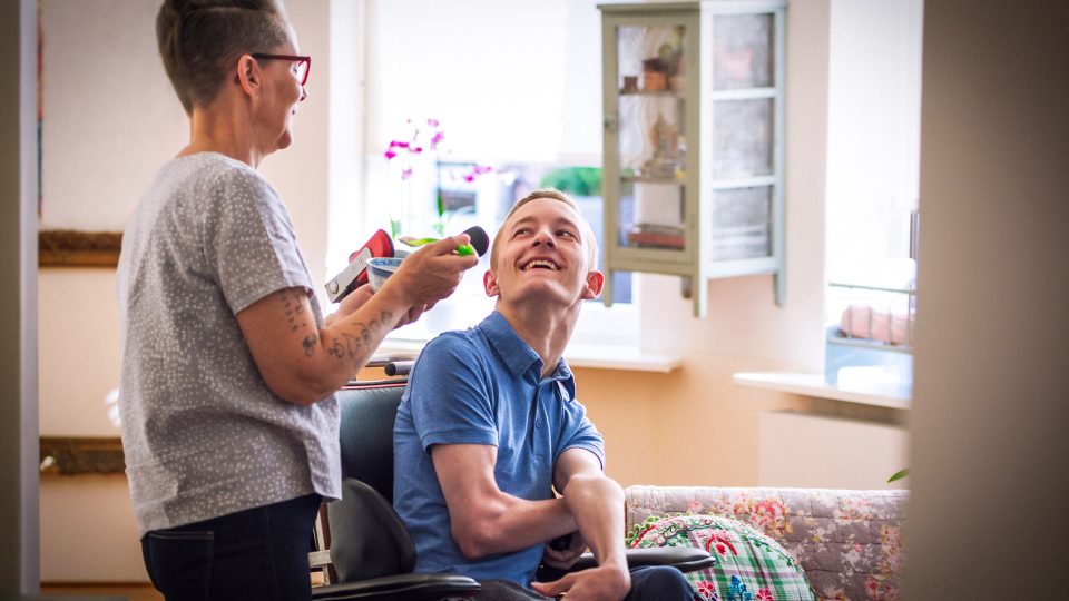 DISABILITY carer help feeding a young man wheelchair bound with cerebral palsy both sharing a laugh together