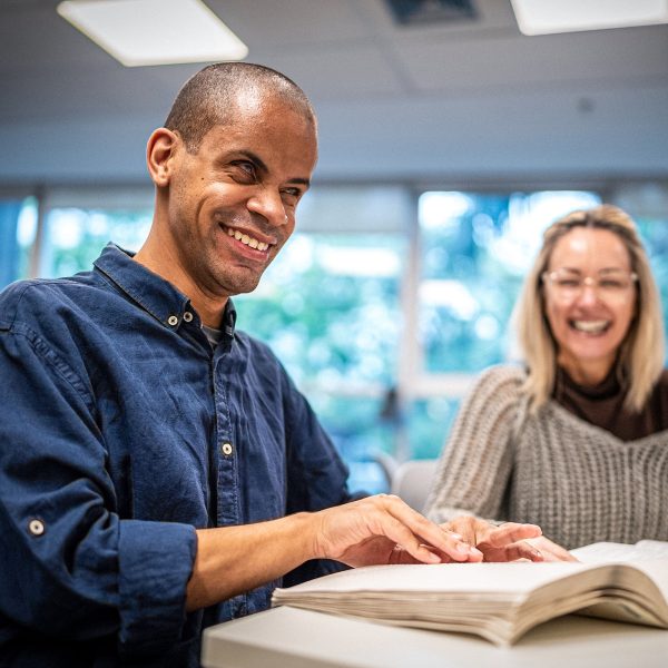 DISABILITY blind young man smiling while reading a braille book next to a female friend