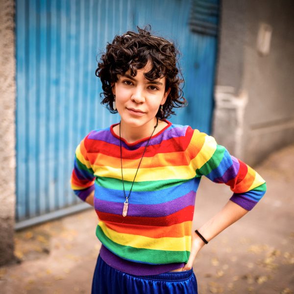 MENTAL HEALTH young adult female staring at the camera with a slight look of defiance and attitude wearing a colourful striped top inspired by LGBTI+ flag