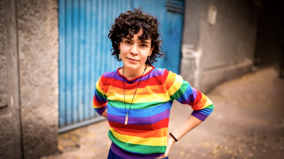 MENTAL HEALTH young adult female staring at the camera with a slight look of defiance and attitude wearing a colourful striped top inspired by LGBTI+ flag