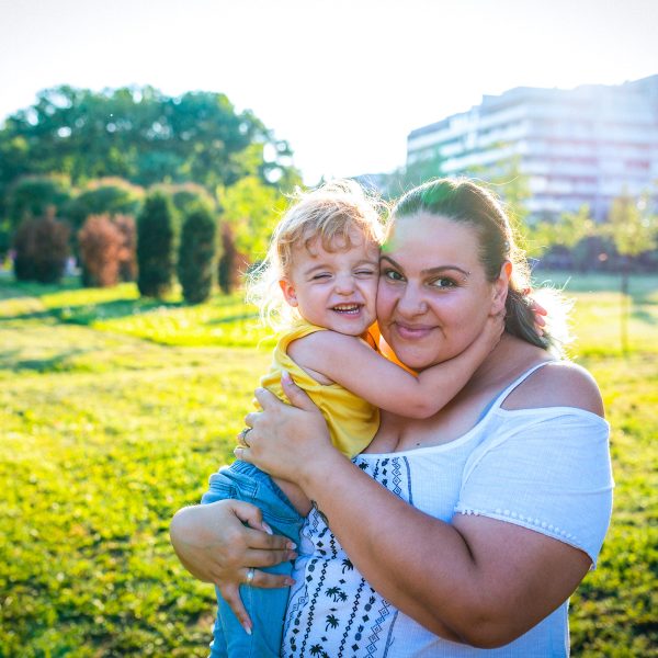 MENTAL HEALTH young mother slightly smiling cuddling her toddler as she looks at the camera, her toddler eyes closed giggling