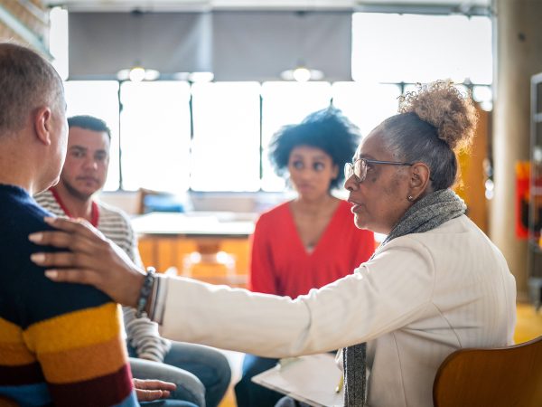 MENTAL HEALTH Woman leading the Horizons group therapy compassion with hand on shoulder of an older male as she listens intently