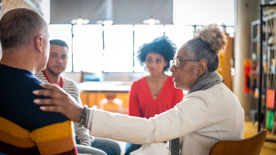 MENTAL HEALTH Woman leading the Horizons group therapy compassion with hand on shoulder of an older male as she listens intently