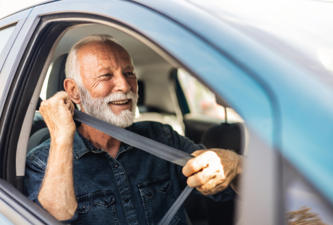 An older man with a beard smiling as he puts his seat belt on ih his car