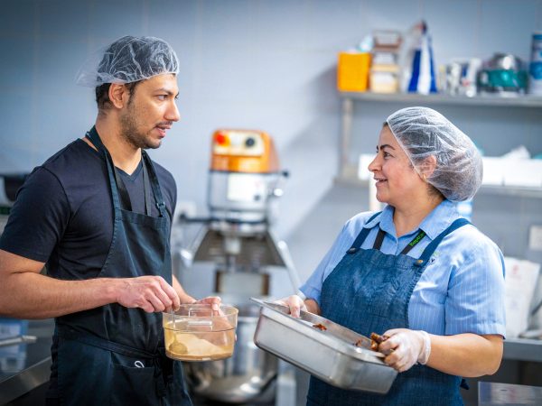 CAREERS Food assistant chatting with cook in kitchen in a residential aged care home wearing hair net