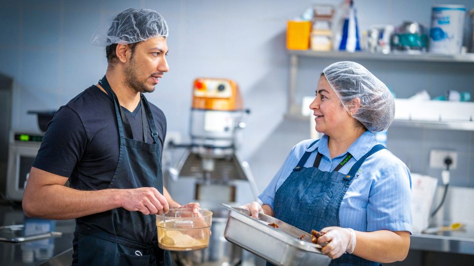 CAREERS Food assistant chatting with cook in kitchen in a residential aged care home wearing hair net