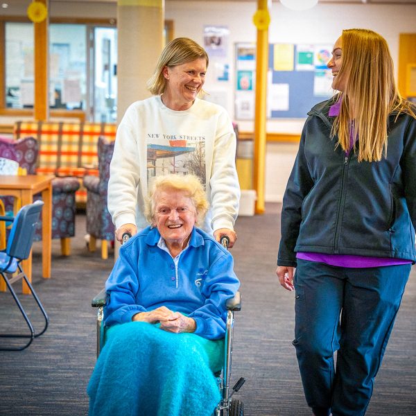 BAPTCARE KARINGAL Resident and daughter with staff member strolling through lounge area chatting and laughing