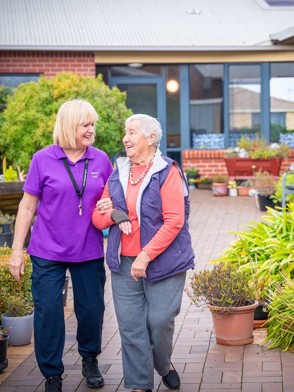 BAPTCARE KARINGAL Resident with staff member outside in courtyard walking sharing a smile