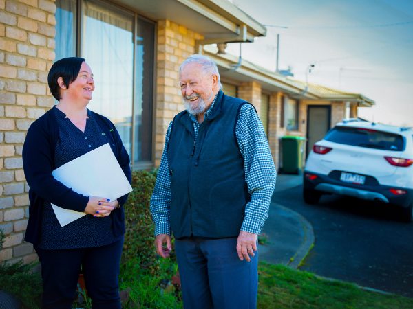 HOME CARE staff member with a customer outside their home chatting with a fleet car in the background collecting them to go to Orana