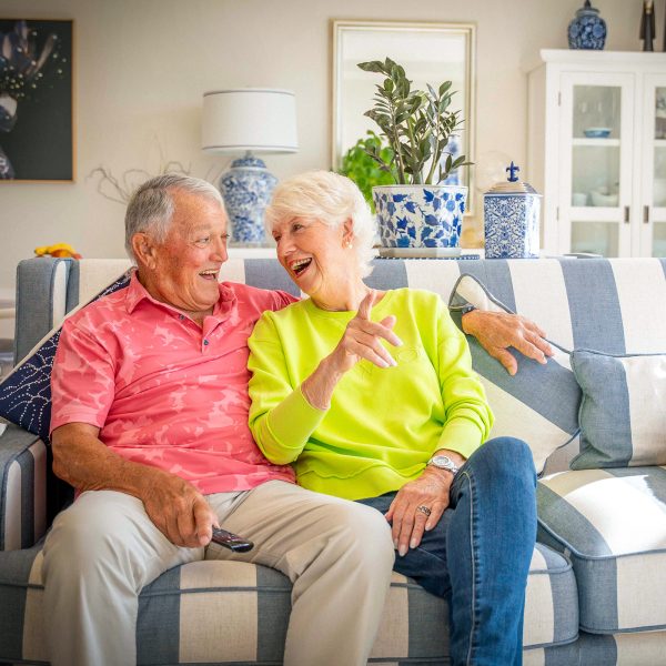 Residents at Peninsula View apartments enjoying their lounge room on the sofa with their dog having a laugh