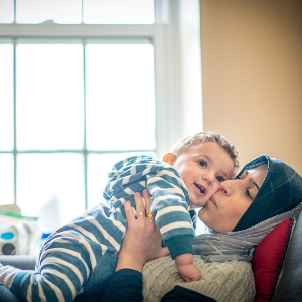 Relaxing mother seeking asylum sharing a playful moment with her smiling infant son kissing him on the cheek