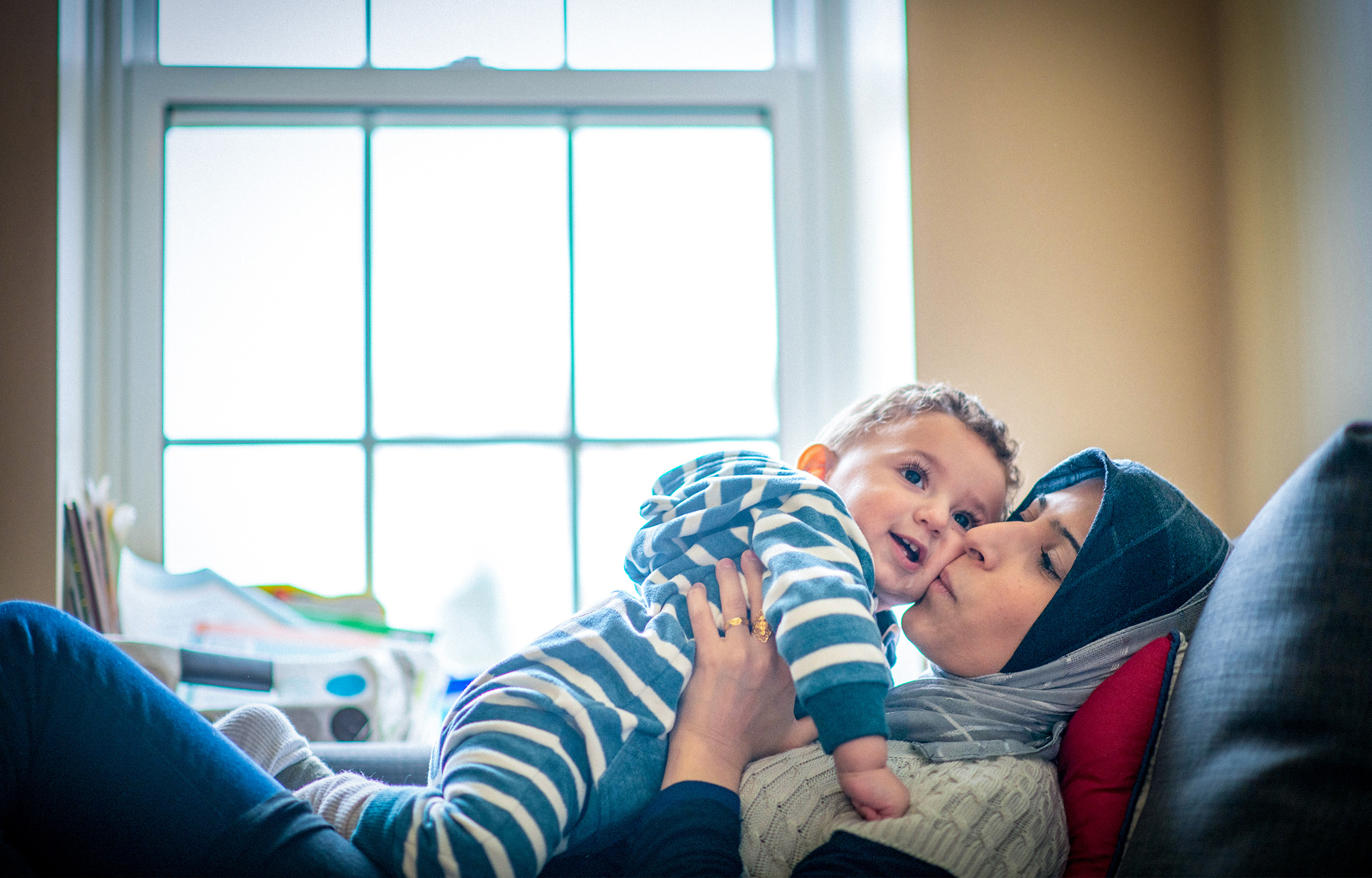 Relaxing mother seeking asylum sharing a playful moment with her smiling infant son kissing him on the cheek