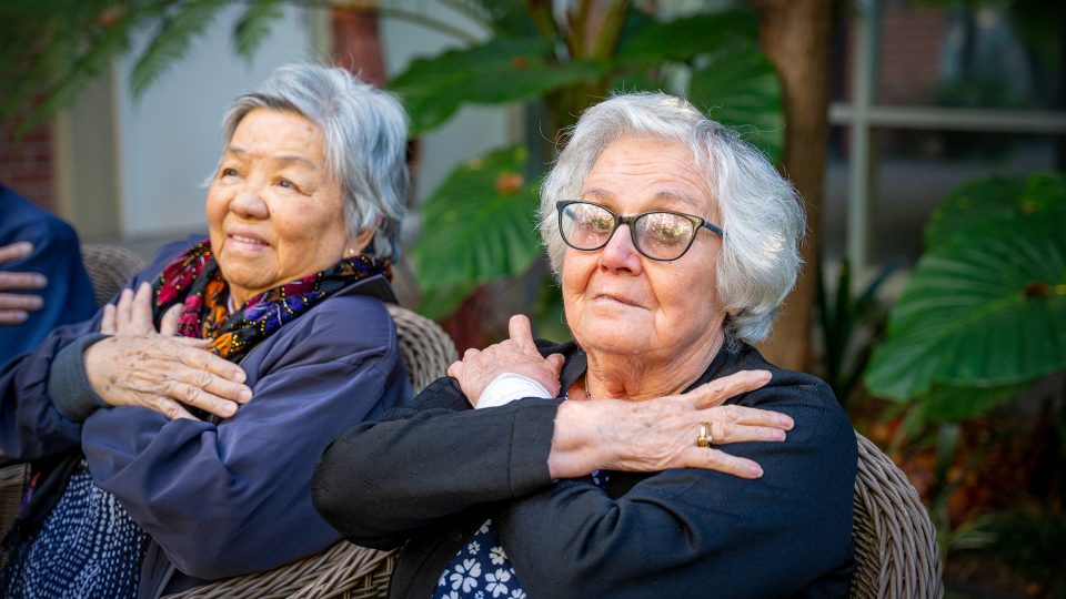 BAPTCARE WESTHAVEN residents doing stretching exercises in chairs outside one resident looking to camera