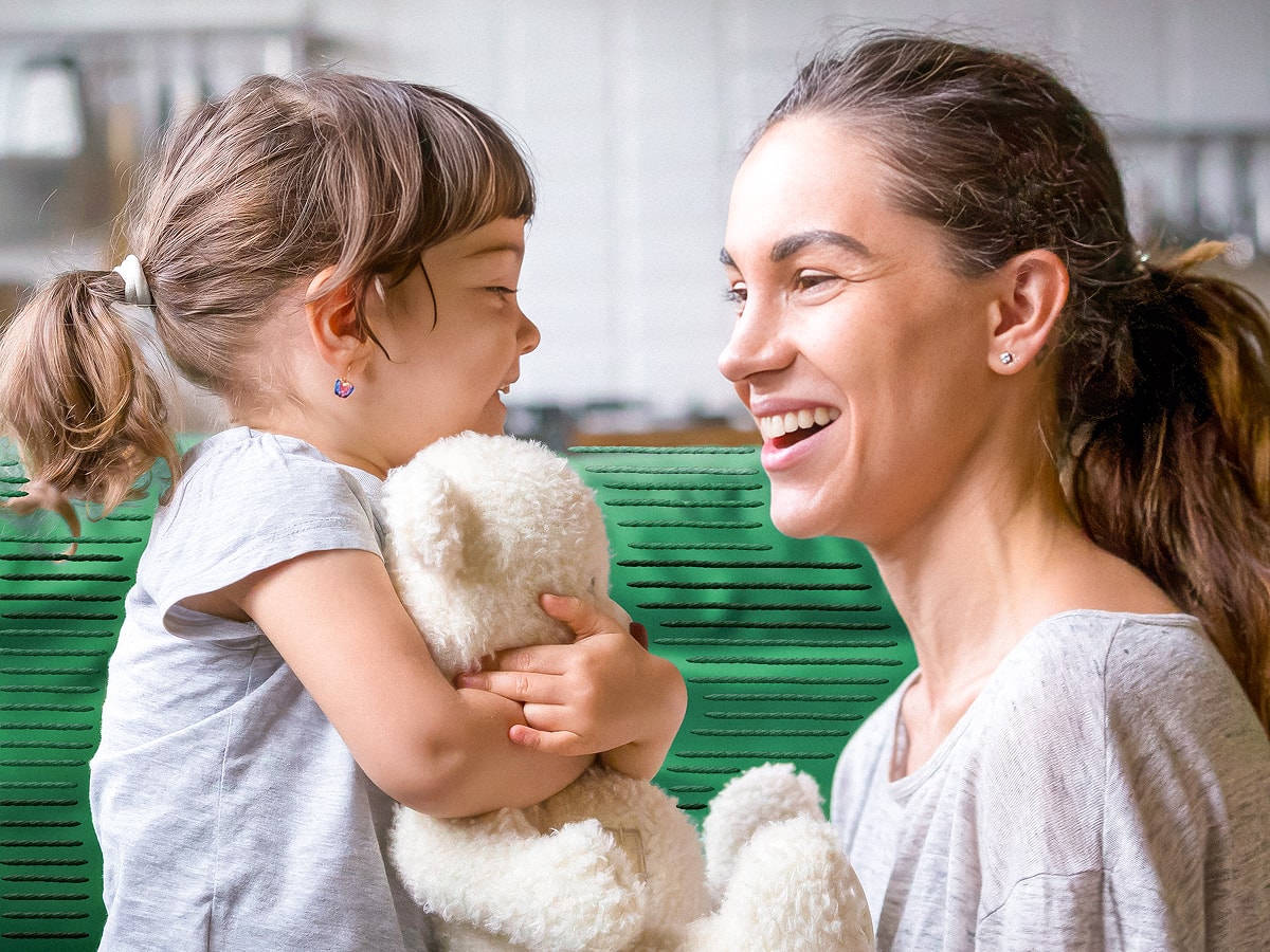 Mother and child smiling at each other while the child holds a teddy bear