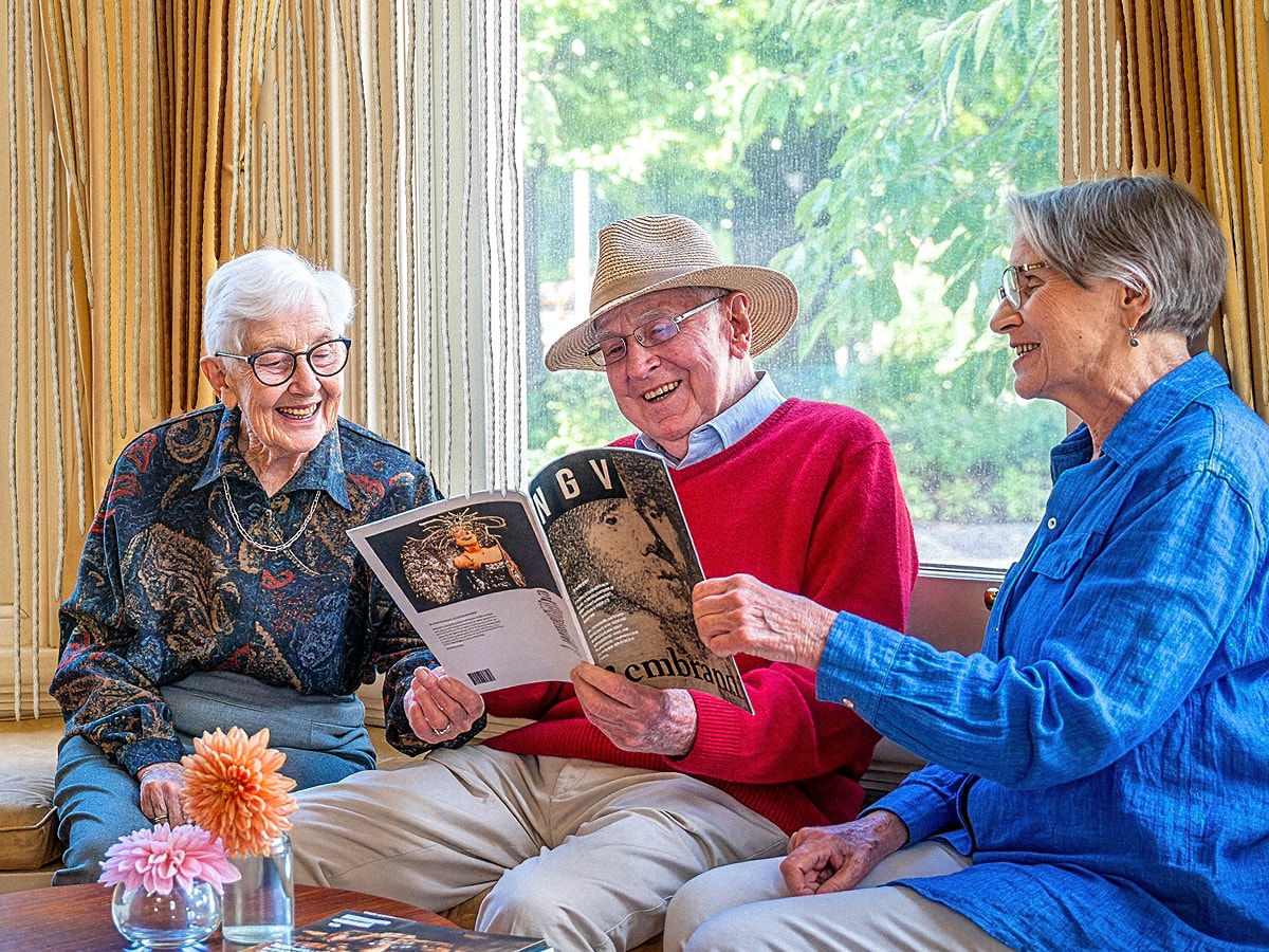 Three friends sitting together smiling over a magazine